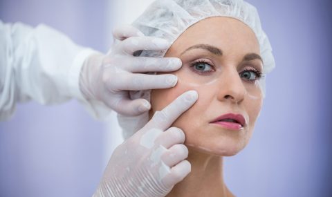 Cosmetic doctor examining woman’s cheeks before dermal filler treatment for volume restoration