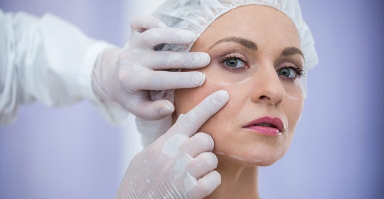 Cosmetic doctor examining woman’s cheeks before dermal filler treatment for volume restoration